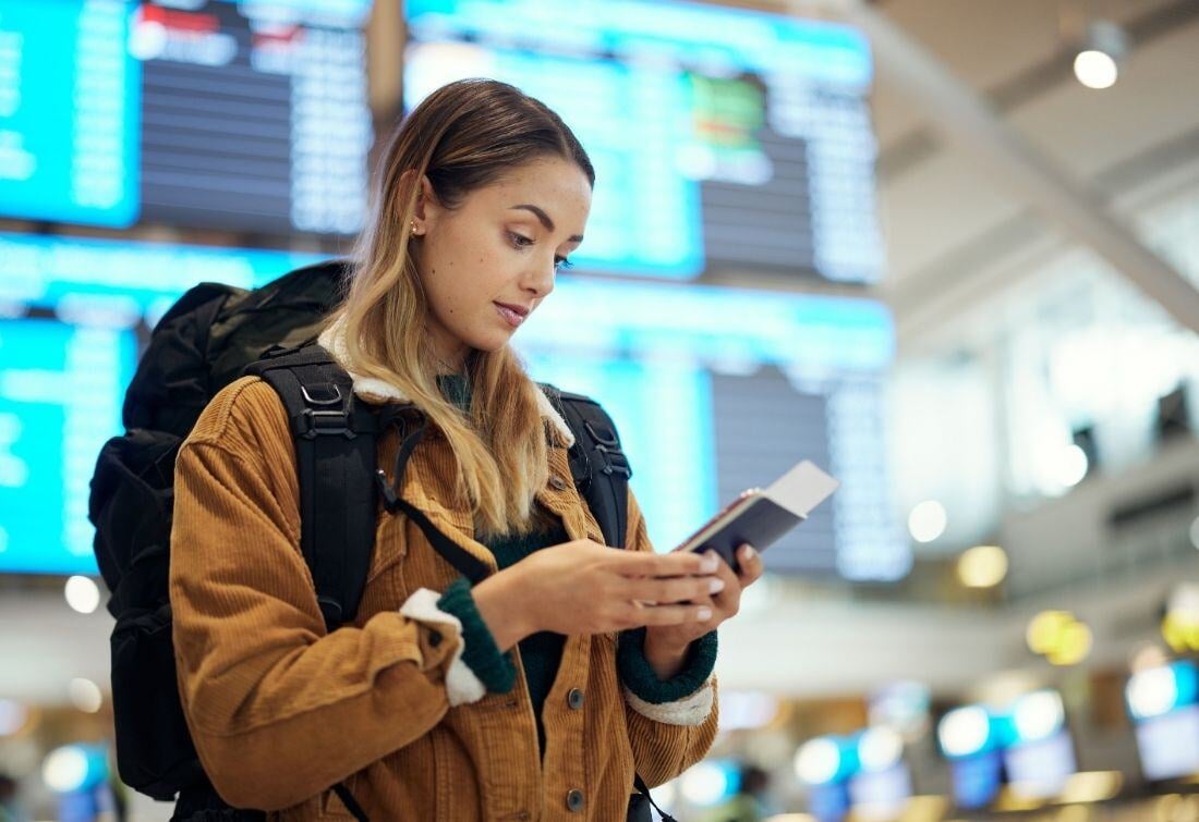 Customer stands in the middle of an airport terminal with her phone, passport, and smartphone needing customer support