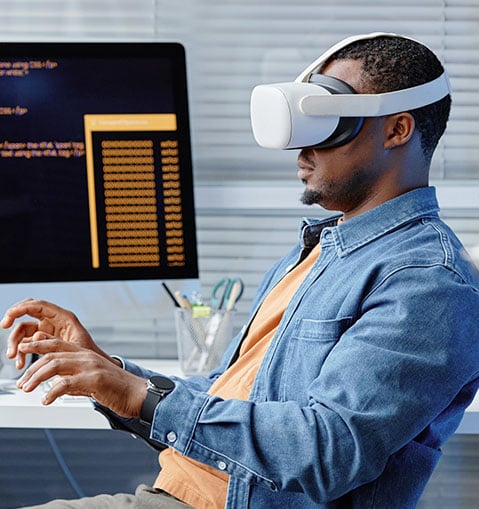 Technical assistant sits at his desk and works on his computer via VR headset