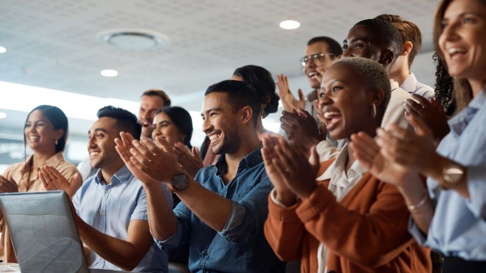 Diverse group of corporate individuals clap and cheer together in an office setting