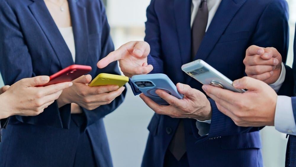 A group of four individuals discuss amongst themselves with four different smart phones in their hands