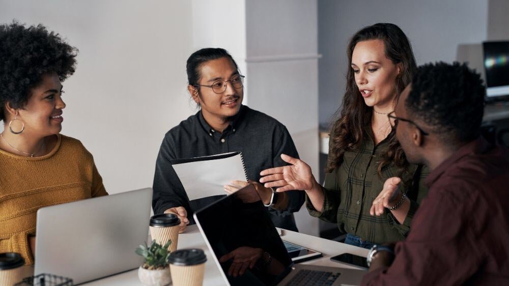 Diverse and intelligent group of individuals group in an office setting to listen to their mentor speak to them in a meeting room