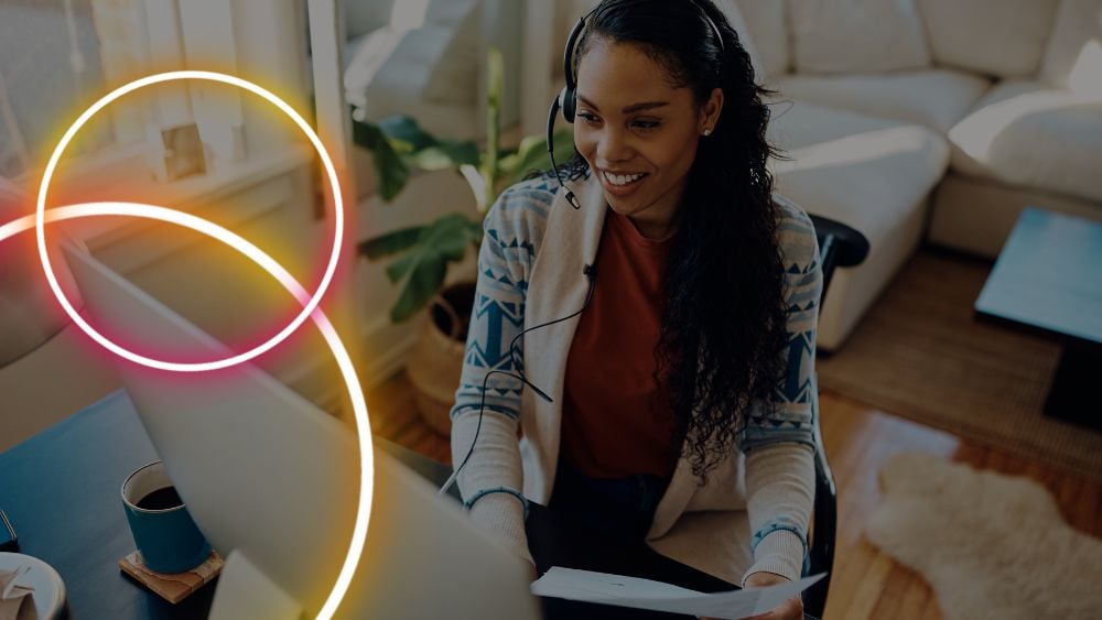 Happy African American woman with headphones having voice call over computer while working at home