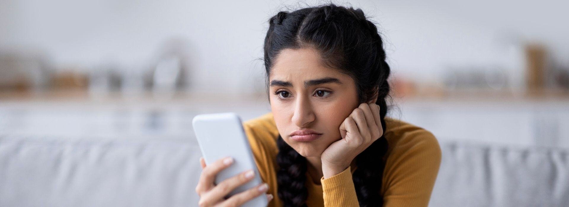 Frustrated customer frowns at her smartphone as she waits for a long time to be connected to customer service