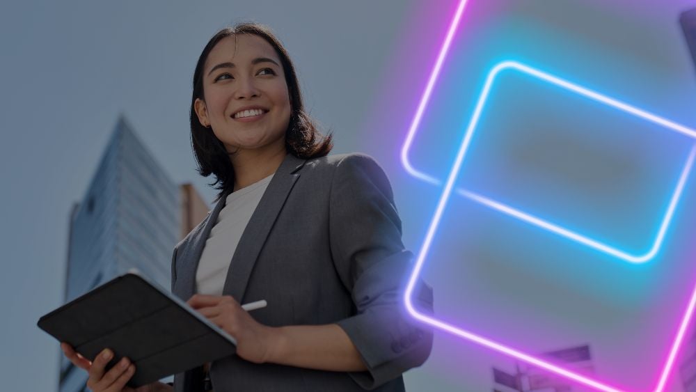 Smiling young Asian business woman leader entrepreneur holding a digital tablet and pen, outside with skyscrapers in the background